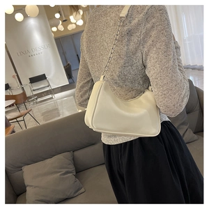 Chic cream-colored hobo underarm bag with metal chain strap worn on person