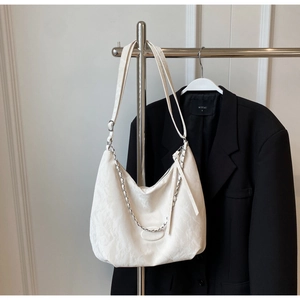 Detail of cream hobo bag showing embossed texture and silver chain strap against a blazer