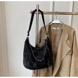 Detail of black wrinkled velvet underarm bag with silver chain and wide shoulder strap