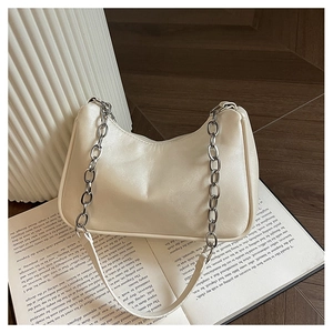 Detail of cream hobo bag with thick silver chain on an open book, minimalist chic