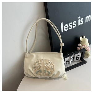 Detail of elegant beige silk shoulder bag featuring floral embroidery and chic tassels