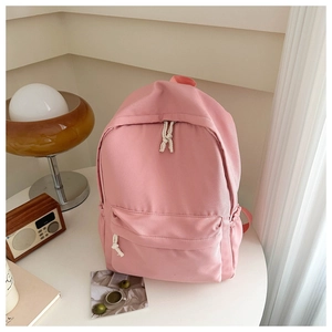 Dettaglio dello zaino rosa minimalista con tiranti bianchi e tasca frontale esterna