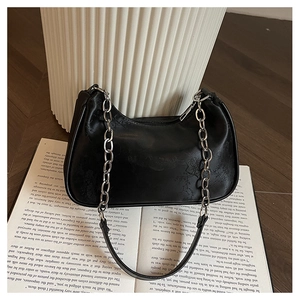 Detail of black underarm bag with subtle pattern, silver chain, and leather shoulder strap