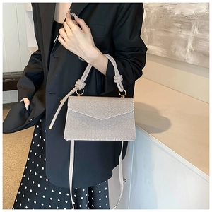 Petit sac bandoulière beige texturé avec anse torsadée porté sur un tailleur noir