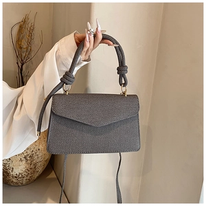 Détail du sac carré gris foncé avec poignée tressée et rabat au design géométrique