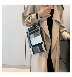 Detail of the chic black and white checkered envelope clutch held by a model in beige coat