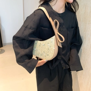 Handwoven green dumpling bag with floral embroidery and cream bow shoulder strap