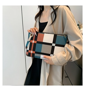 Detail of color-block plaid clutch with gold ring handle and leather wrist strap