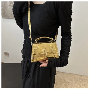 Detail shot of a mini golden stone pattern handbag worn by a model in black outfit