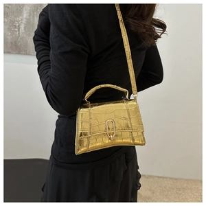 Detail of gold crocodile-patterned crossbody bag with elegant metal clasp and handle