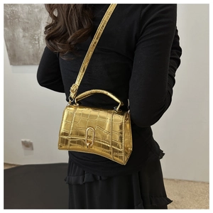 Detail view of golden crocodile embossed mini bag with metallic finish on a black outfit