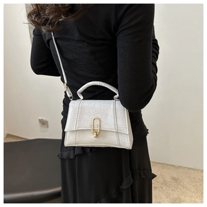 White crocodile pattern crossbody bag with gold buckle worn on the shoulder by a model