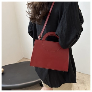 Model wearing dark red leather crossbody bag in a minimalist interior setting
