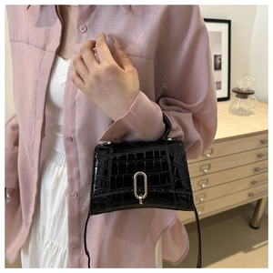 Detail of glossy black crocodile pattern handbag with elegant oval golden metal clasp