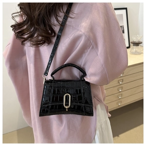 Detailed shot of black crocodile embossed handbag with gold buckle on shoulder strap