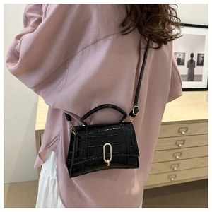 Detail of black faux crocodile skin handbag with elegant golden metal U-shaped buckle