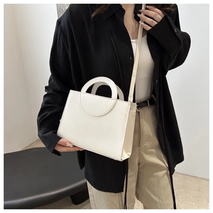Close-up of minimalist white square crossbody bag with circular hollow handle detail