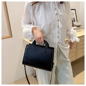 Chic black matte leather crossbody bag held by a model in a casual outfit
