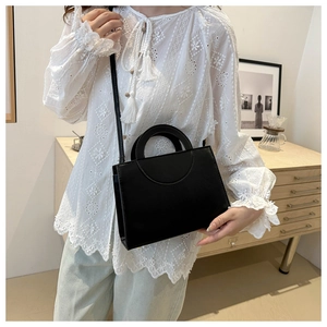 Detail of a black minimalist leather crossbody bag with a round handle on a model