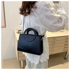 Detail view of a black leather handbag with gold metal hardware on a stylish female model