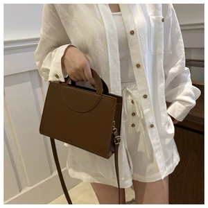 Brown rectangular crossbody bag with round cutout handle styled on a white linen outfit