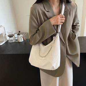 White crescent tote bag with silver chain detail shown on shoulder in cafe setting