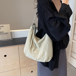 Large beige pleated hobo bag with chain strap shown on a model in professional attire