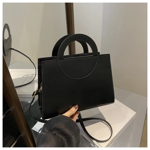 Detail of minimalist black PU leather bag with circular cutout handle and detachable strap