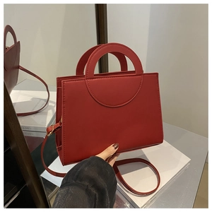 Detail of red PU leather handbag with unique circular cutout handle and crossbody strap