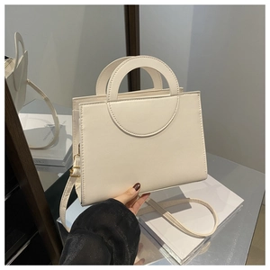 Close-up of cream leather handbag featuring a unique semicircular handle and gold hardware