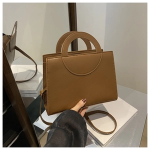 Close-up of brown leather handbag featuring unique circular cutout handle and strap