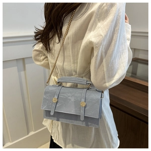 Détail du sac à main bleu clair plissé avec bandoulière chaîne dorée sur tenue blanche
