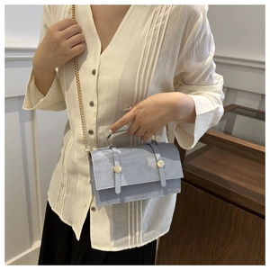Detail of light blue crossbody bag with embossed texture and gold chain strap worn by model