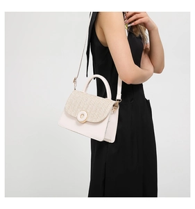Detail of the woven texture and golden lock on a cream-colored crossbody handbag