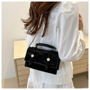 Detail of black pleated texture handbag with golden chain and silver metal buttons