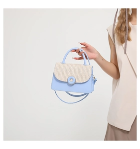 Detail of blue leather shoulder bag with straw weave flap and round buckle accent
