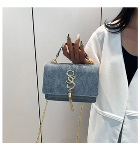 Detail of blue denim shoulder bag with golden S-buckle and long tassel pendant
