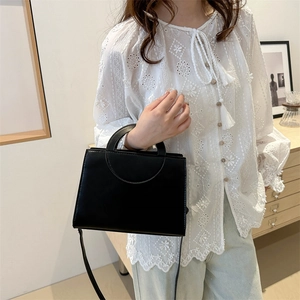 Minimalist black leather crossbody bag with semi-circular handle in modern interior setting