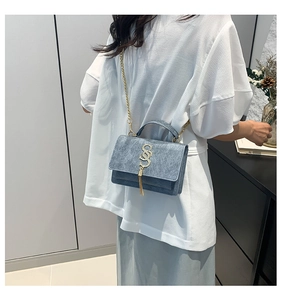 Detail of blue textured crossbody bag with gold S-buckle, fringe tassel and chain strap