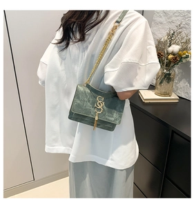 Close-up of dark green suede crossbody bag with gold tassel and metal logo