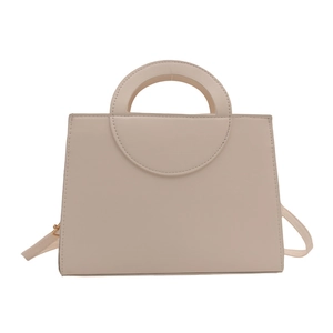 Minimalist beige structured trapezoid handbag with circular cutout handle and shoulder strap