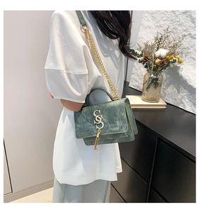 Detail of dark green suede handbag featuring golden snake logo and fringe tassel charm