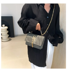 Detail of grey suede square bag featuring a gold S-shaped buckle and metal chain strap