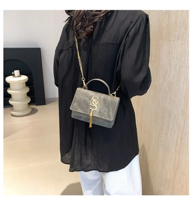 Detail of grey-green suede crossbody bag with gold hardware and tassel on model