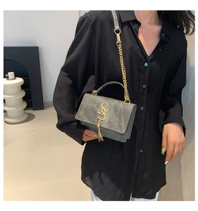 Detail of grey-blue shoulder bag with golden S-buckle and tassel on a female model