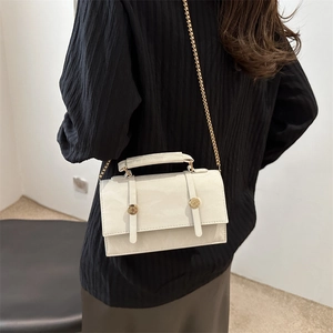 Sac à bandoulière gris clair minimaliste avec chaîne dorée porté par un modèle