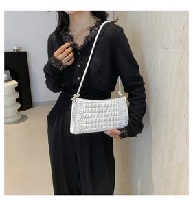 Detail of white crocodile texture underarm bag on a model in a minimalist modern setting