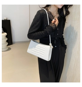 Detailed side view of white crocodile pattern shoulder bag worn by model in soft lighting