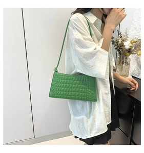 Close-up of vibrant green crocodile-embossed underarm bag with unique knotted strap detail