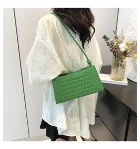 Detail of green croc-embossed underarm bag with knot strap on a white shirt